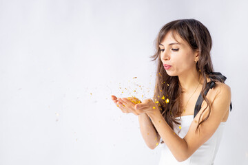 Wall Mural - a happy young girl holding blows golden confetti off her hands and enjoys the holiday on a white isolated background, space for text