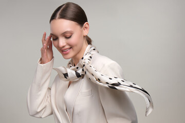 Wall Mural - Close up portrait of a beautiful elegant woman with stylish jewelry on a white gray background. Girl in white jacket with scarf