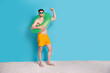 © deagreez - Full size photo of attractive young man hold float circle raise fist excited wear trendy yellow shorts isolated on blue color background