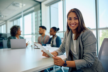 Young happy businesswoman using touchpad during meeting in office and looking at camera.