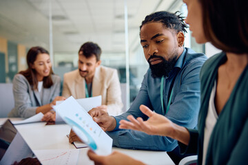 Wall Mural - Black entrepreneur analyzing business charts with coworker on meeting in office.