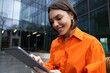© zinkevych - Smiling girl in orange shirt with a device looking contented
