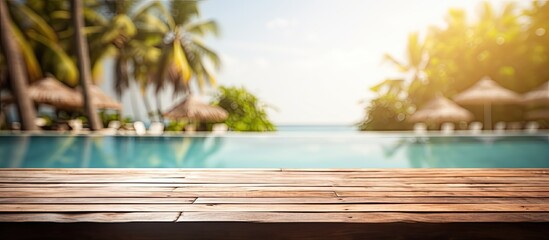 Wall Mural - Blurry background image of a brown wooden table near a poolside on a beach resort