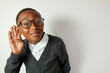 Studio portrait of schoolboy in glasses eavesdropping holding hand around right ear, wearing funny round eyeglasses, listening to rumors with curiosity against foot space background