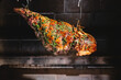 © Andrew Kornylak - A leg of lamb covered in herbs hangs roasting over hot coals in a rustic brick outdoor oven