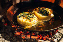 Cheese And Herbs Roasting In A Steel Pan Over Hot Coals