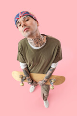 Wall Mural - Tattooed young man with skateboard on pink background