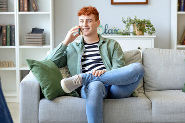 Wall Mural - Young redhead man talking by mobile phone on sofa at home