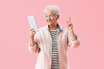 Senior woman with tablet computer pointing at something on pink background