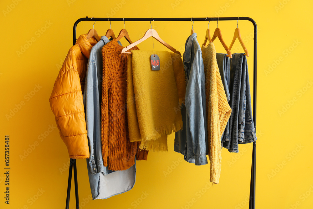 Rack with different clothes against yellow background. Black Friday sale