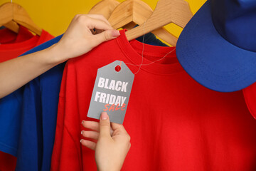 Poster - Female hands with sale tag and clothes on yellow background, closeup. Black Friday