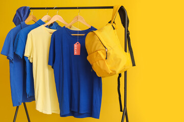 Poster - Rack with t-shirts, cap and backpack on yellow background. Black Friday sale