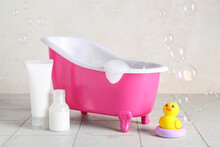 Small Bathtub With Foam, Cosmetic Products And Duck On Light Tile Table