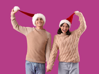 Wall Mural - Happy young couple in Santa hats on purple background