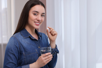 Poster - Beautiful young woman with glass of water and pill indoors, space for text