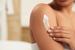 © New Africa - Young woman applying body cream onto arm in bathroom, closeup. Space for text