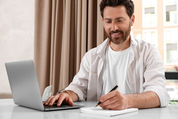 Wall Mural - Man working on laptop and writing something at table in cafe