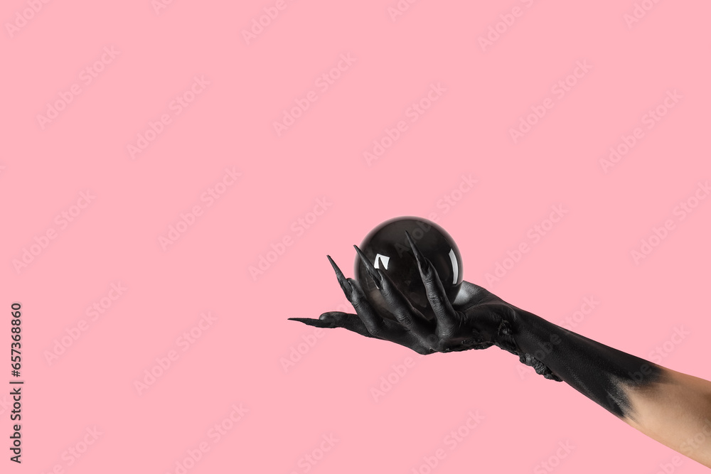 Black hand of witch with crystal ball on pink background. Halloween celebration