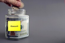A hand putiing coins in money glass jar with written sticky note REINVEST, concept of growing investment by planning to reinvest  interest/ income/yield in profitable investment to gain more profit