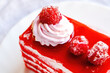 Fresh homemade Red Velvet cake decorated with whipped cream and raspberry berries on white plate close up.