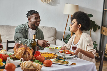 happy african american woman passing plate with cooked meal to relative during Thanksgiving dinner