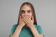 Embarrassed woman covering mouth with hands on grey background