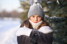 Portrait of beautiful girl young frozen pretty woman standing walking in winter snowy park at cold snow frosty day in hat, scarf, in gloves looking at camera
