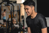 A young handsome asian man grunts while doing tricep pushdowns at the gym.