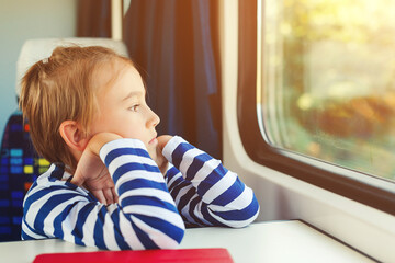 Little boy is traveling on the train. Kid travels on a train. Cute child looking out the train window.