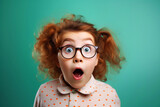 Fototapeta  - Excited, shock, omg wow expression. Shocked surprised funny elementary school kid girl in glasses looking at camera, sitting on bright green background. Promo offer banner, adverts concept