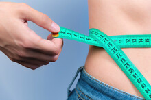 Woman Measures Her Waist With A Tape Measure. Diet And Body Weight Control Concept, Close-up, Toned. A Girl In Jeans Takes Measurements Of Her Figure And Weight Loss