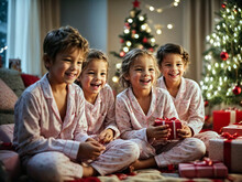 Laughing Children Sit In Their Pajamas In Front Of The Christmas Tree With The Wrapped Presents