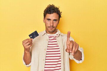 Man holding credit card on yellow showing number one with finger.