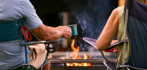 Wall Mural - Rear View Close Up Of Senior Couple Camping In Countryside With RV Drinking Coffee By Outdoor Fire