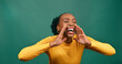 © Meeko Media - Young Black woman raises hands to mouth, yell excitedly, green background studio