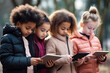 © serperm73 - A multiethnic group of schoolchildren are looking attentively at their gadgets, smartphones and tablets.