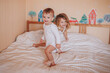 © Natalia Trunova - Two little kids, brother and sister, both dressed in white are jumping on a bed covered with a white blanket