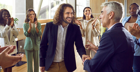 Two happy cheerful business man shaking hands celebrating success, making deal, business achievement, signing contract or greeting new employee with group of people applauding in the office.