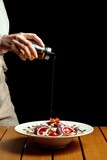 Fototapeta Na drzwi - view of a waitress's hand dressing a salad on the table, black background, 