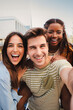 © Jose Calsina - Vertical portrait of a happy multicultural friends laughing taking a selfie together. Mixed teenage cheerful students having fun and hanging out. Young multiracial joyful people looking at camera