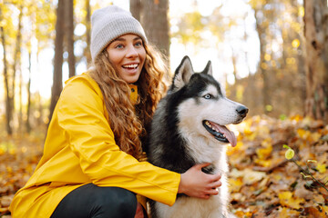 Wall Mural - Beautiful young woman in a yellow coat walks in an autumn park with her pet husky. A pet owner spends time with her dog. Concept of fun, entertainment.