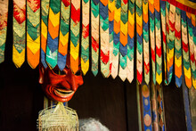 Mask Displayed In A Farmhouse Behind Hanging Colorful Decorative Fabric; Paro Valley, Bhutan