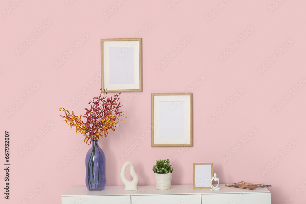 White sideboard with decor and blank frames near pink wall