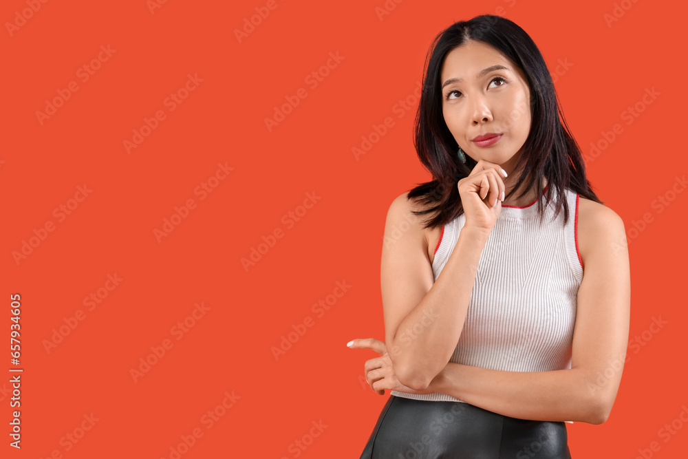 Thoughtful young beautiful Asian woman on orange background