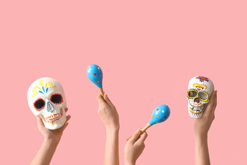 Sticker - Female hands holding painted human skulls for Mexico's Day of the Dead (El Dia de Muertos) and maracas on pink background