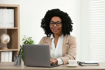 Poster - Happy young woman using laptop at wooden desk indoors