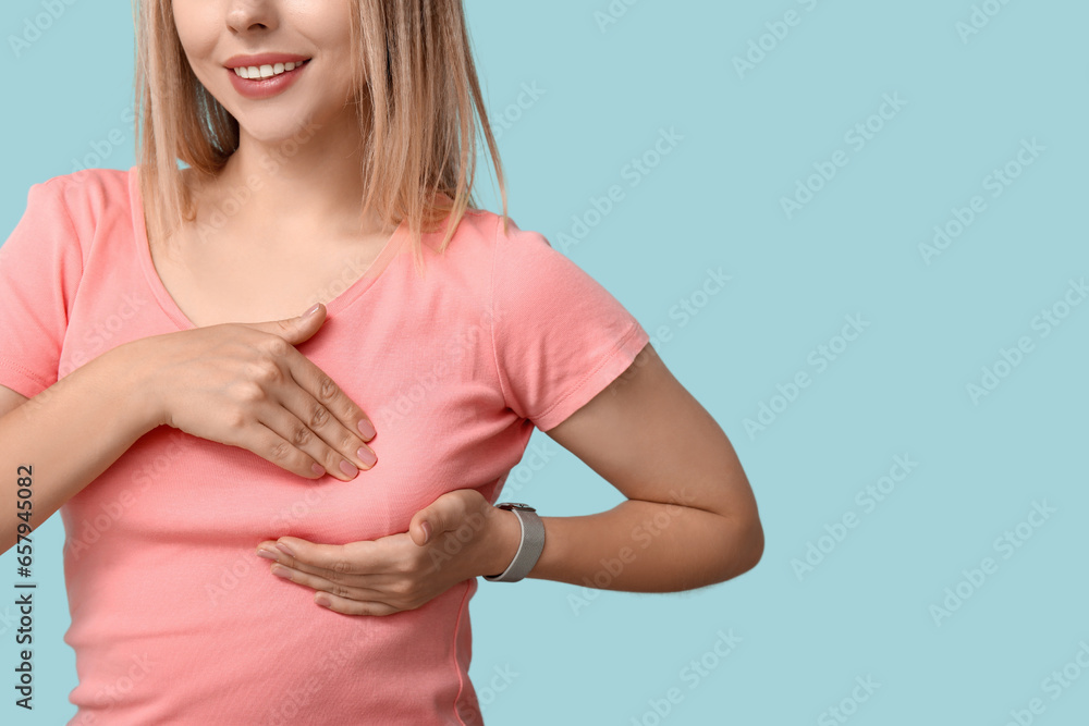 Young woman checking her breast on blue background. Cancer awareness concept
