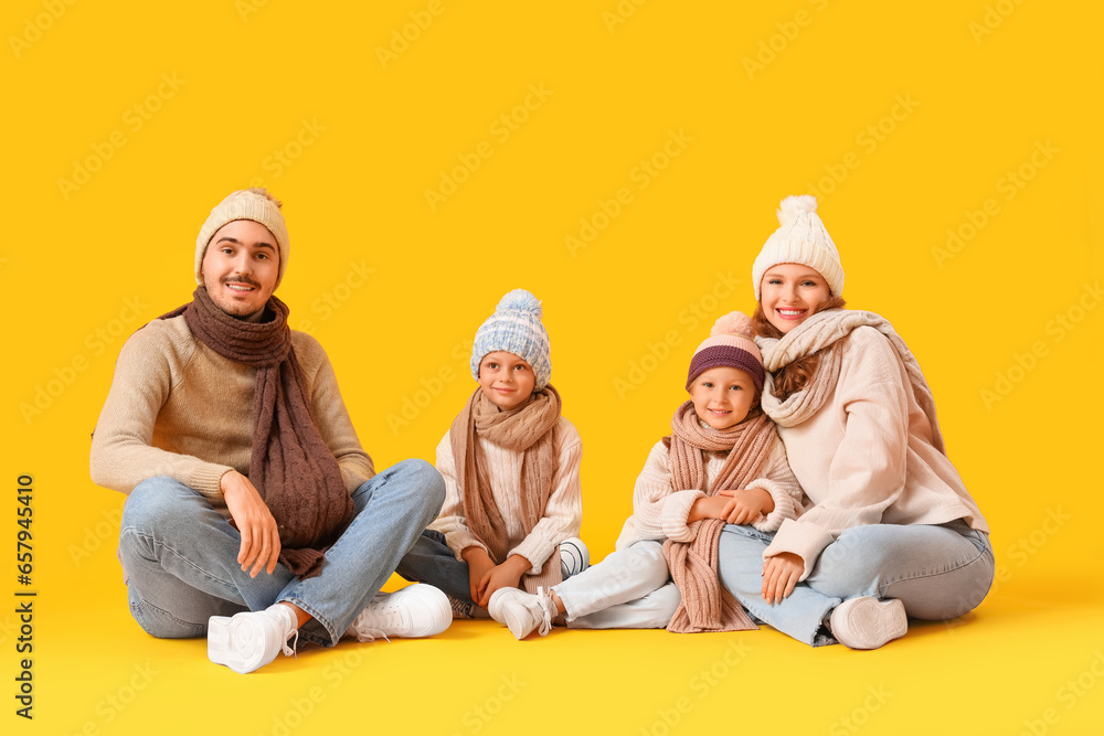 Happy family in winter clothes sitting on yellow background