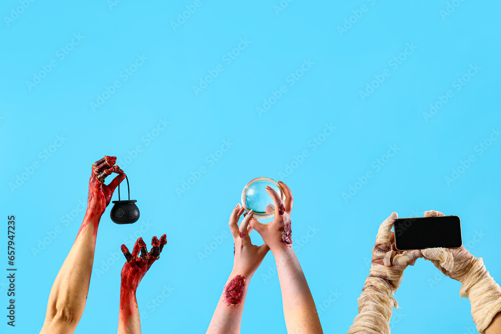 Zombie hands holding cauldron, crystal ball and mobile phone with blank screen on blue background. Halloween celebration