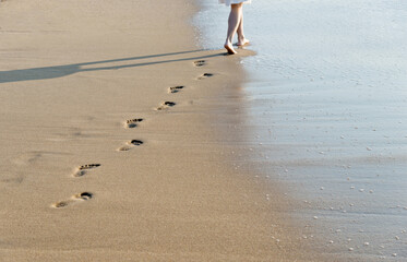 Poster - Woman walking on beach leaving footprints in the sand.